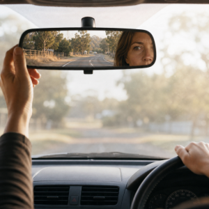 The Long Way Back midlife reflection guide beside a rear-view mirror reflecting a long, quiet road through a muted Australian landscape.
